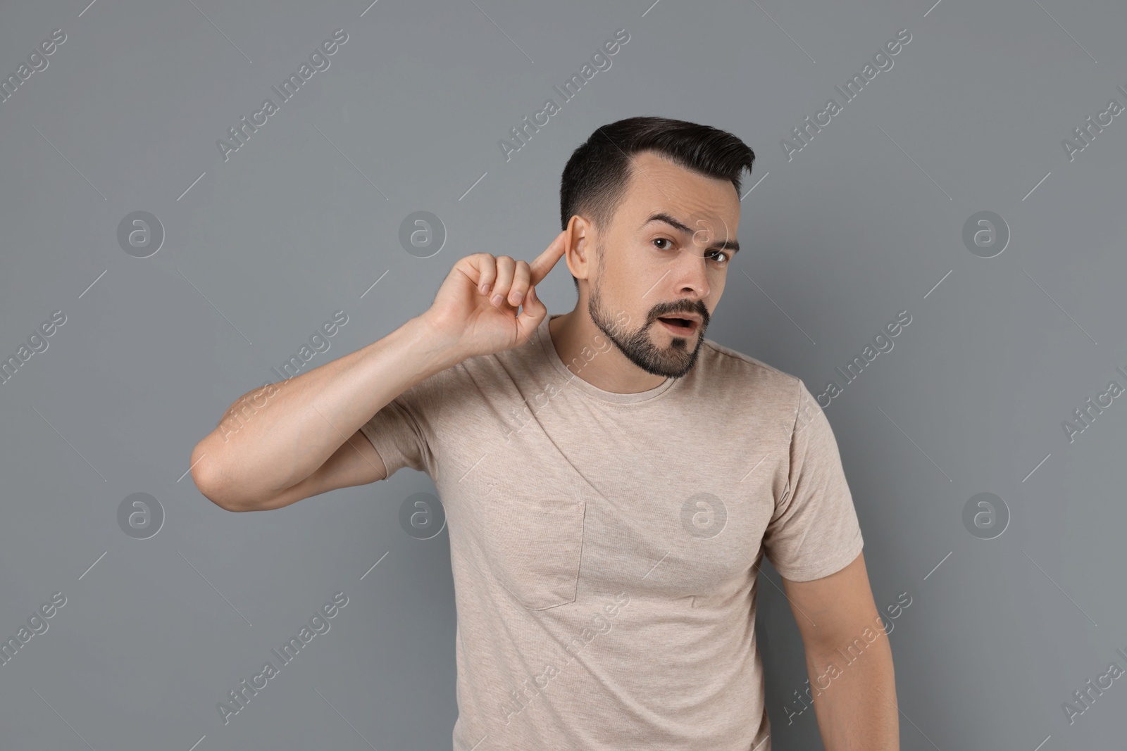 Photo of Man showing hand to ear gesture on grey background