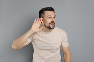 Photo of Man showing hand to ear gesture on grey background