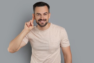 Photo of Man showing hand to ear gesture on grey background