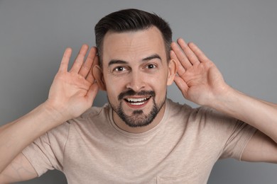 Photo of Man showing hand to ear gesture on grey background