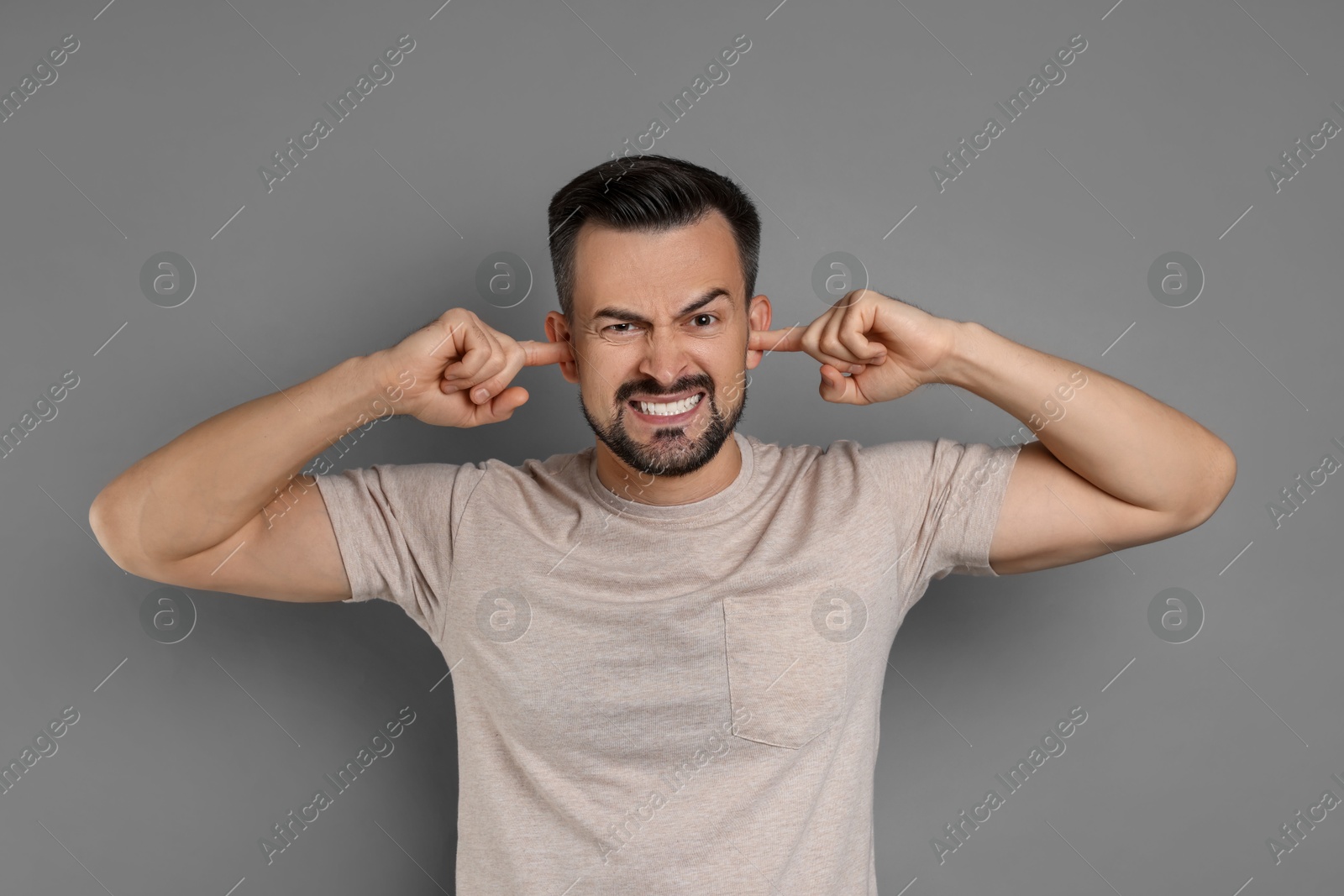 Photo of Man covering his ears with fingers on grey background