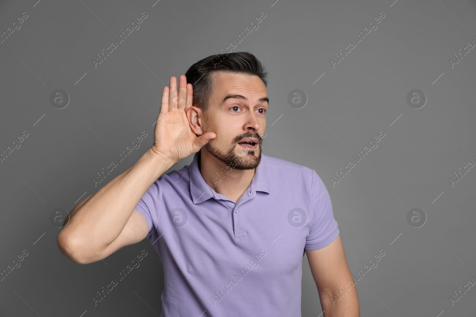 Photo of Man showing hand to ear gesture on grey background