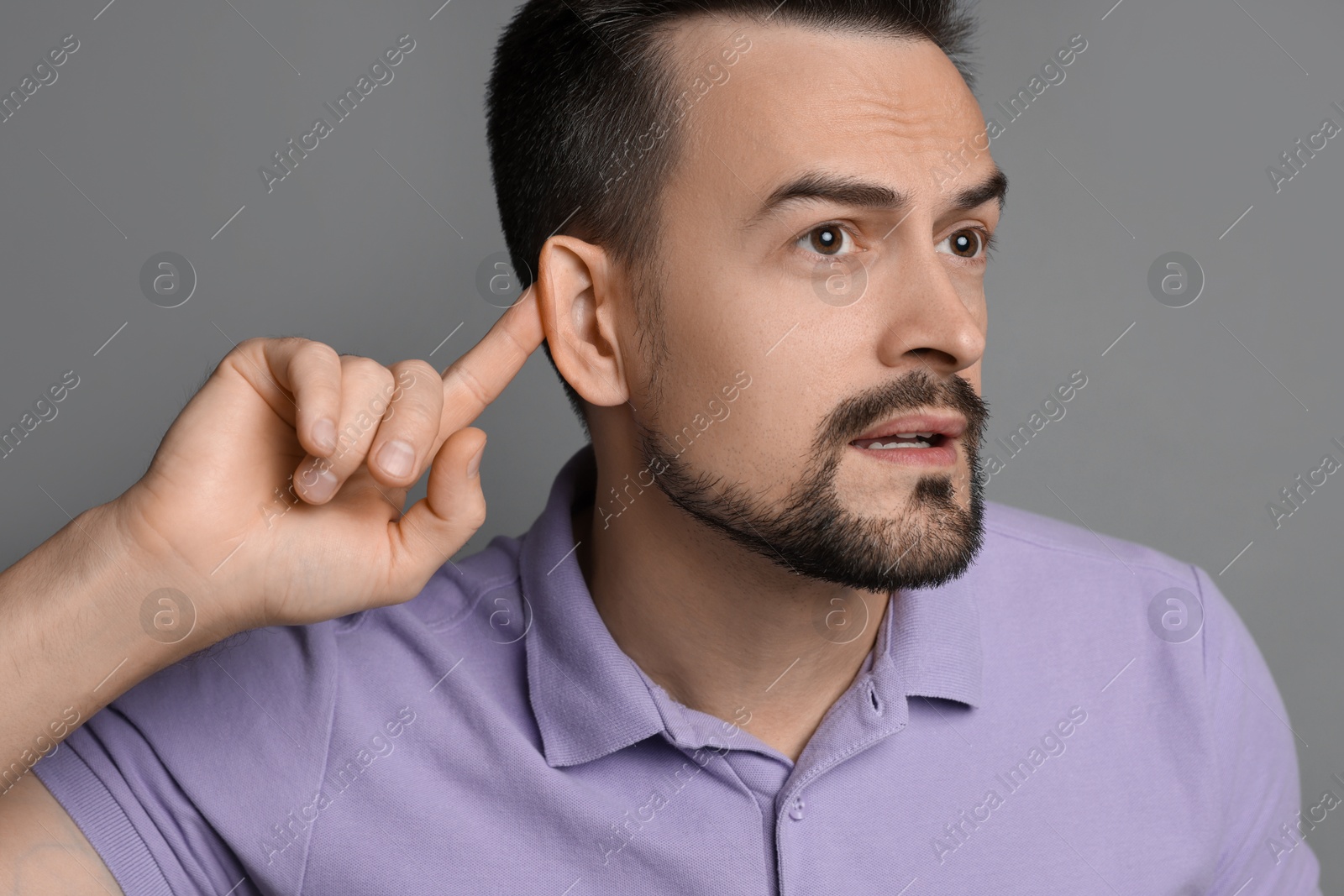 Photo of Man showing hand to ear gesture on grey background