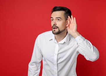 Photo of Man showing hand to ear gesture on red background