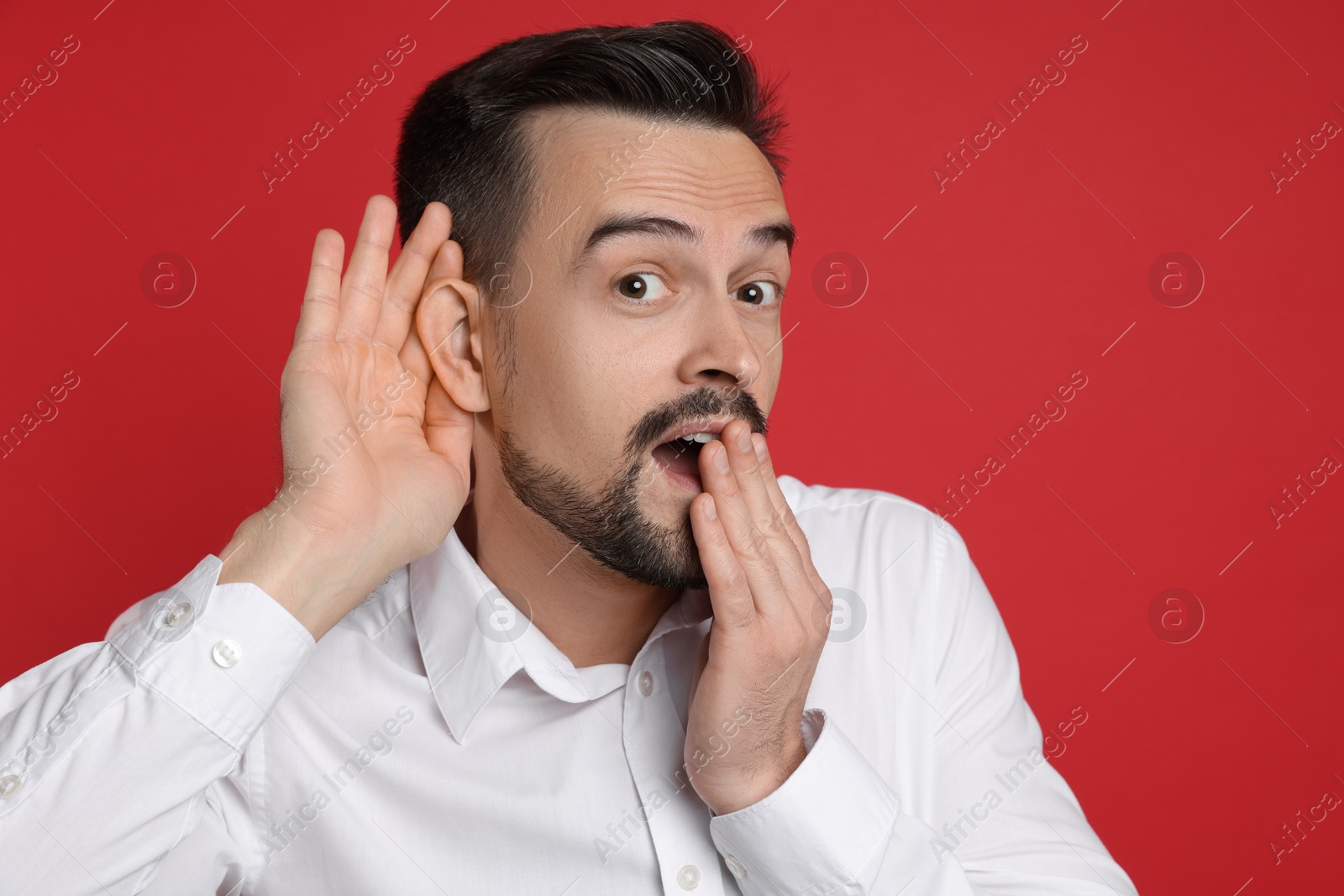 Photo of Man showing hand to ear gesture on red background