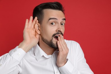 Photo of Man showing hand to ear gesture on red background