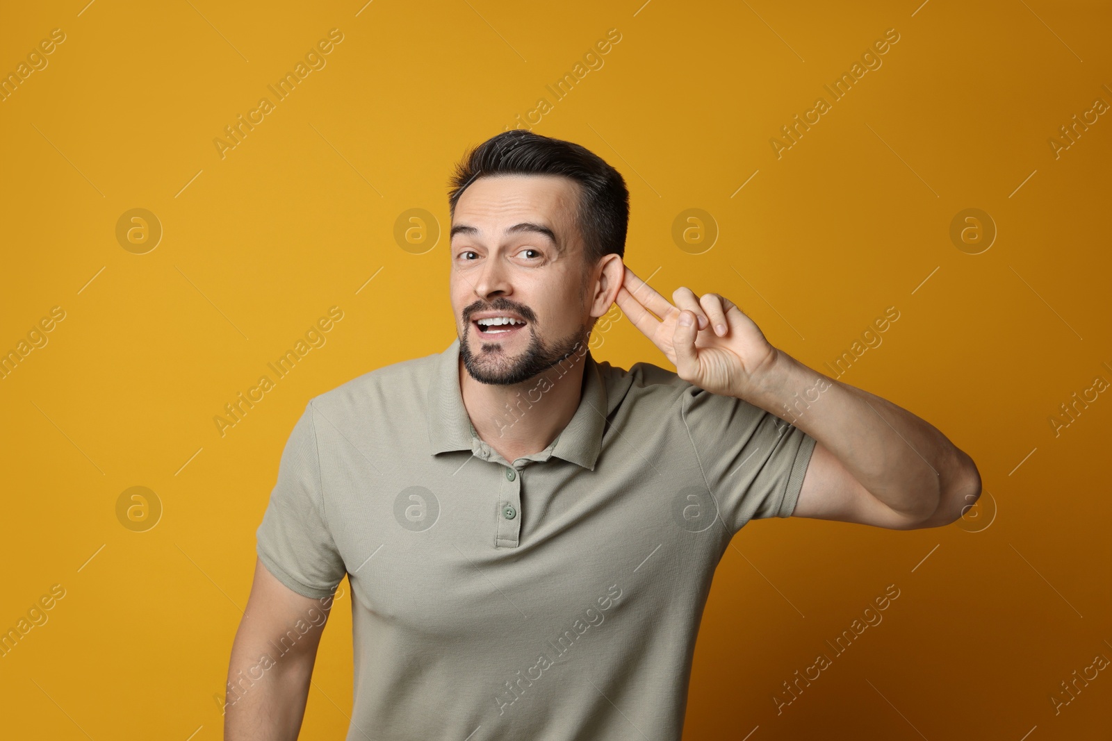 Photo of Man showing hand to ear gesture on orange background