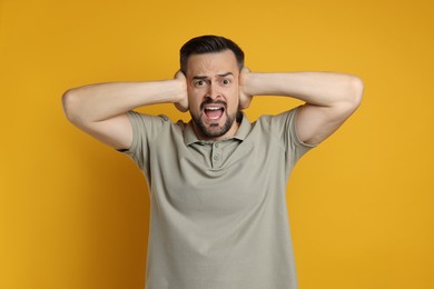 Photo of Man covering his ears on orange background