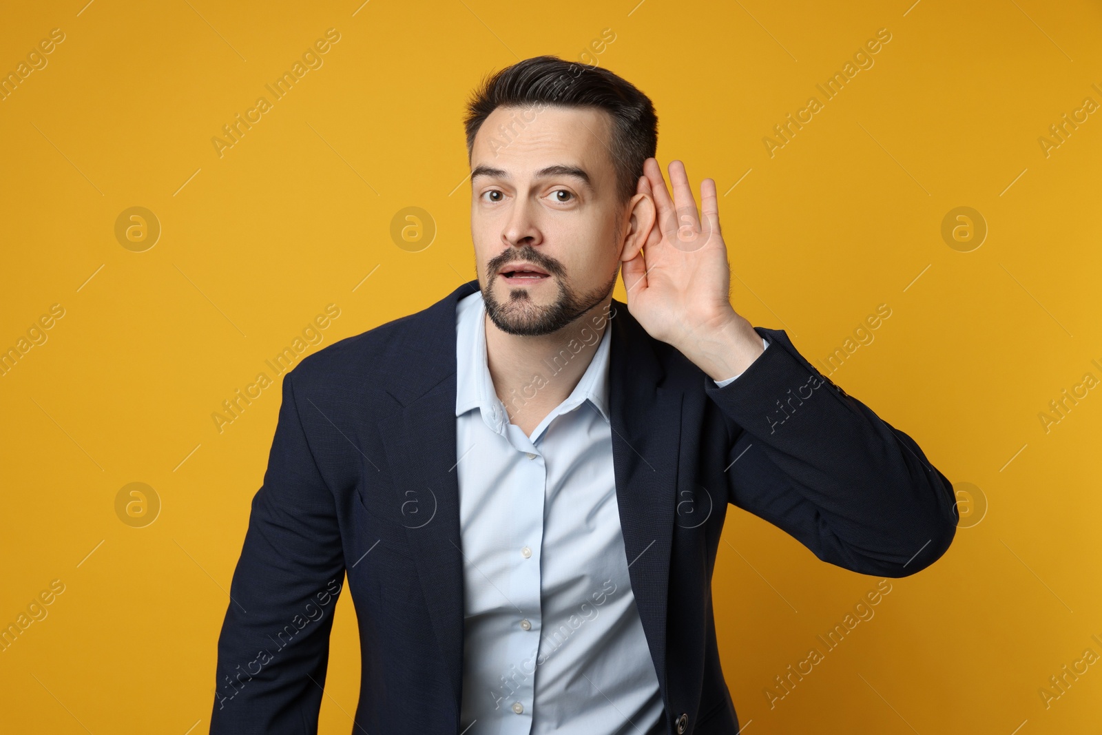 Photo of Man showing hand to ear gesture on orange background