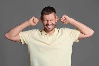 Photo of Man covering his ears with fingers on grey background