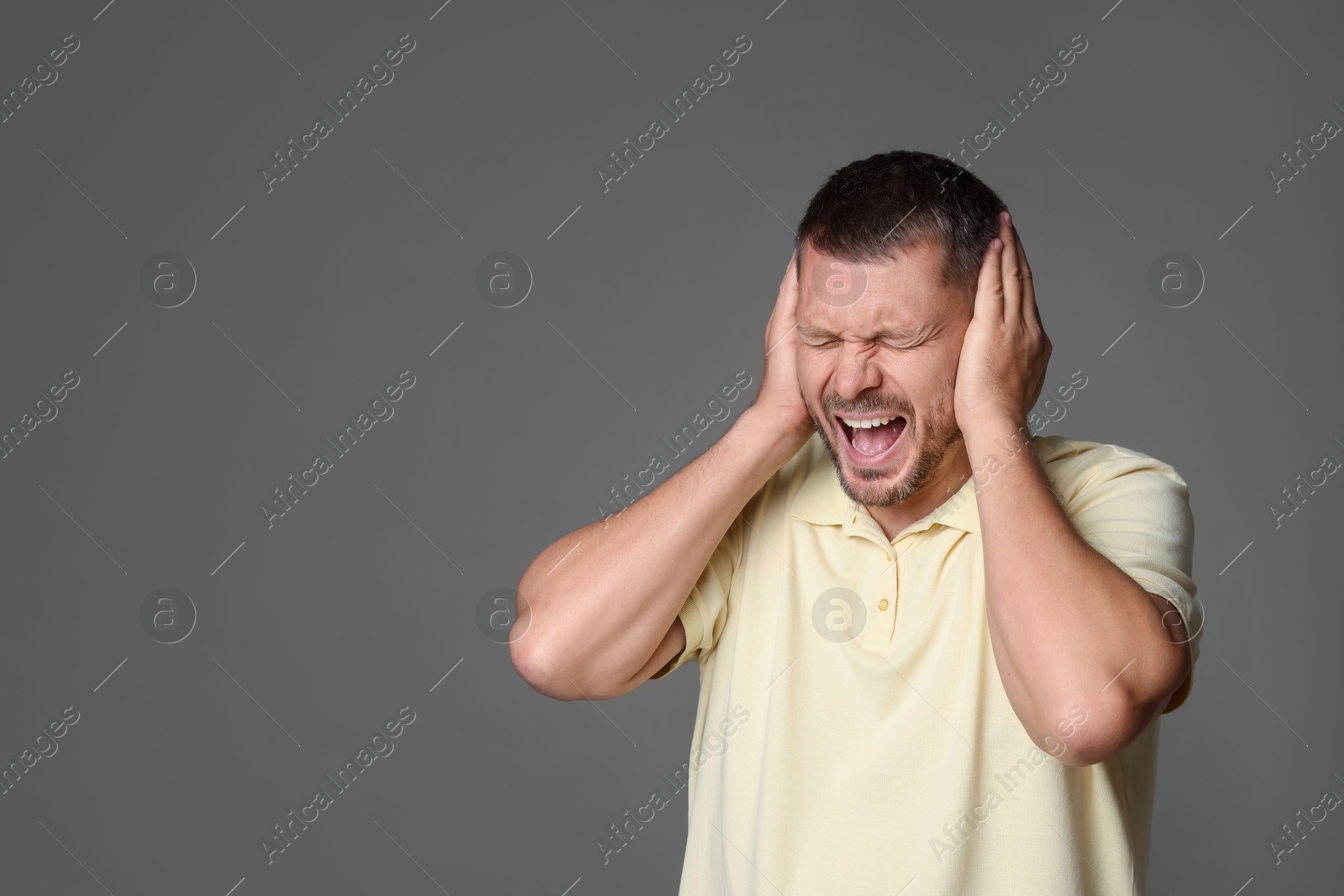 Photo of Man covering his ears on grey background, space for text