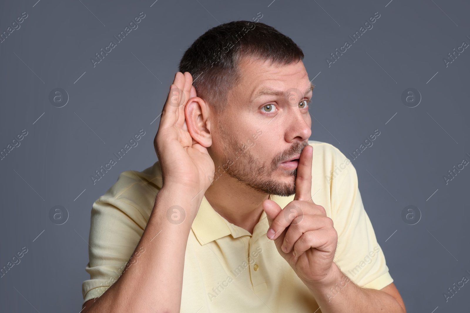 Photo of Man showing hand to ear gesture on grey background