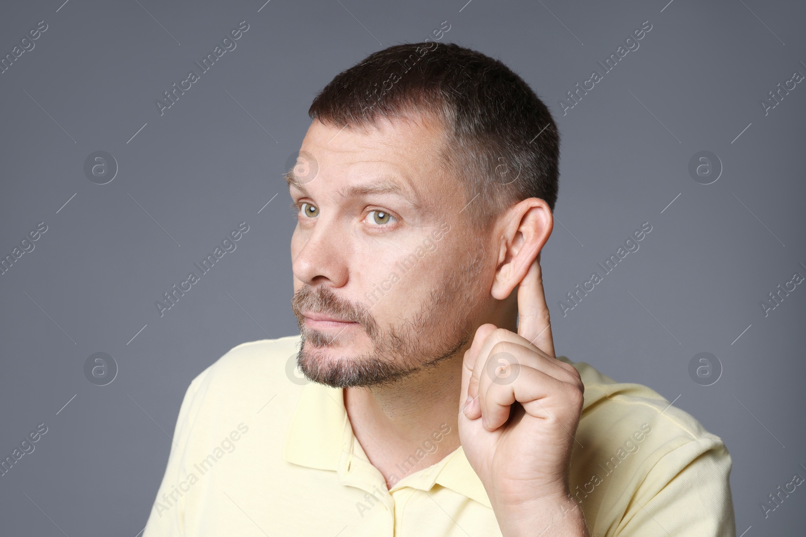 Photo of Man showing hand to ear gesture on grey background