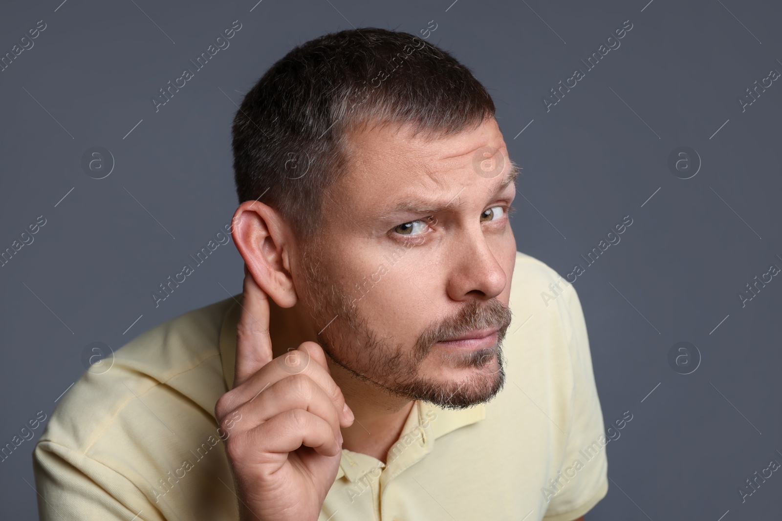 Photo of Man showing hand to ear gesture on grey background