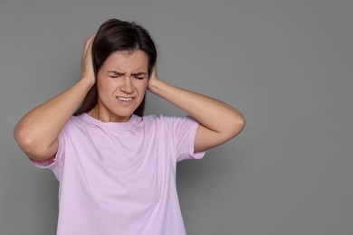 Photo of Woman covering her ears on grey background, space for text