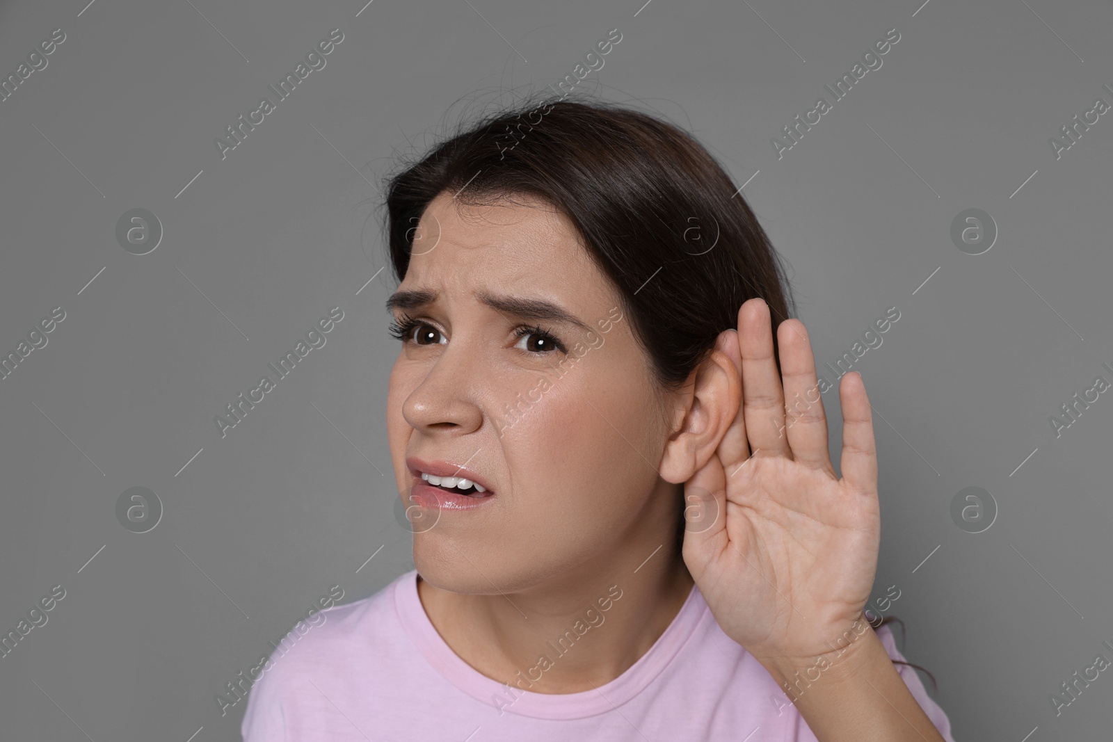 Photo of Woman showing hand to ear gesture on grey background