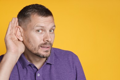 Photo of Man showing hand to ear gesture on orange background, space for text