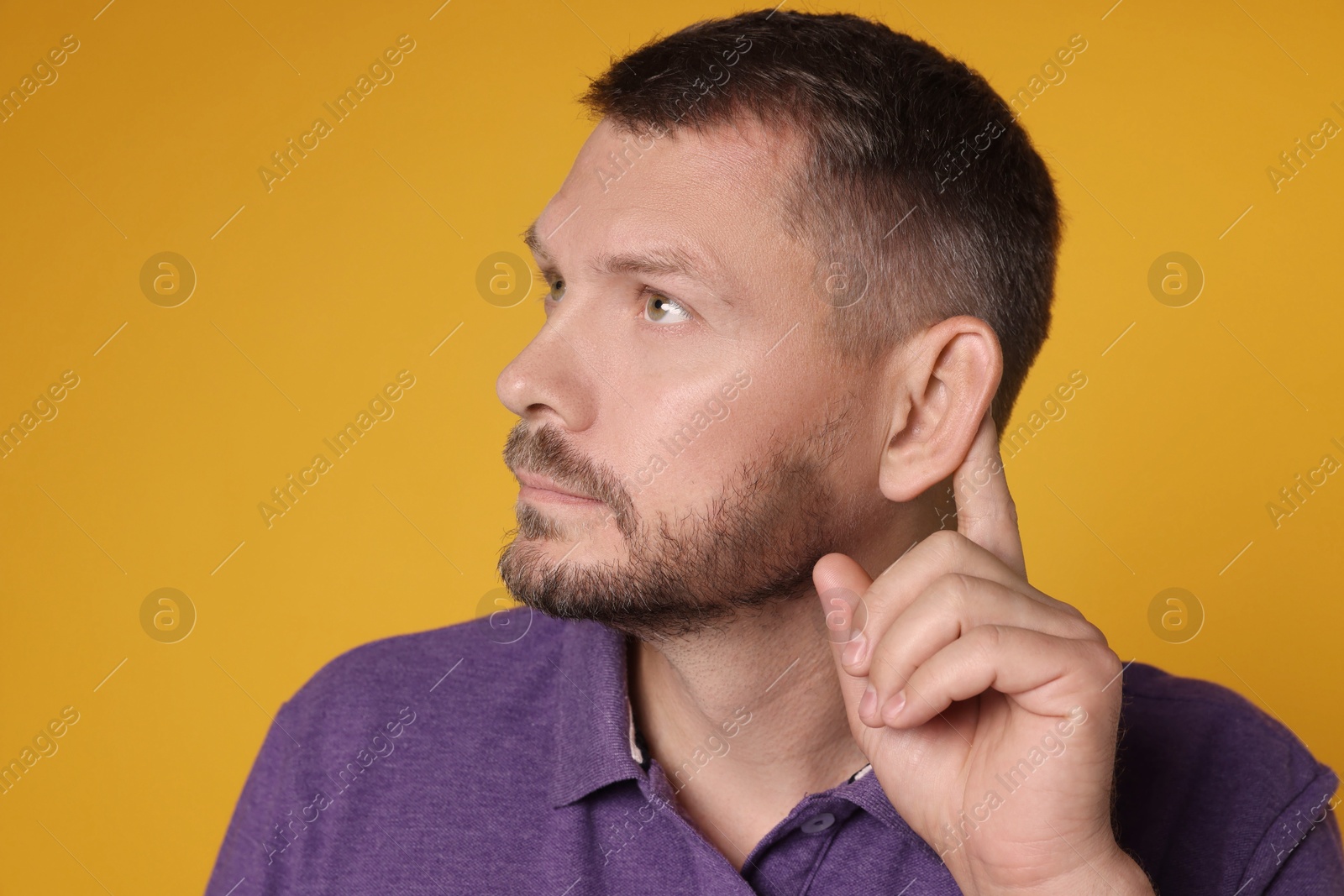 Photo of Man showing hand to ear gesture on orange background