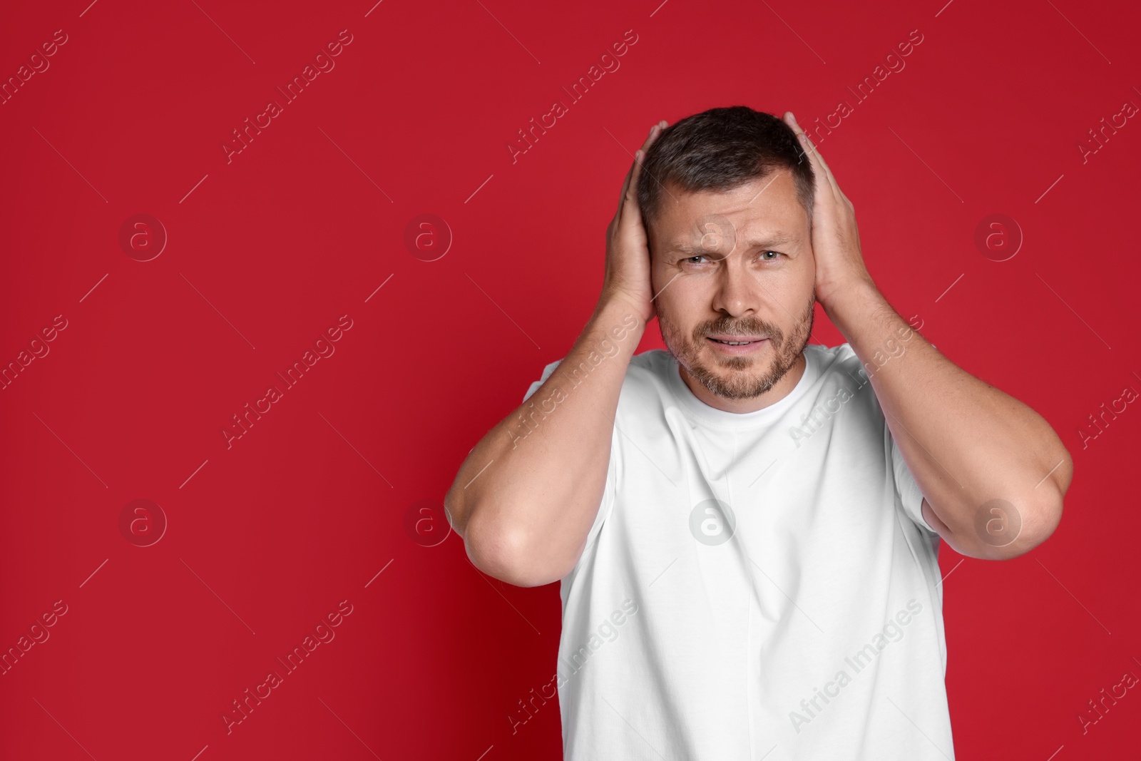 Photo of Man covering his ears on red background, space for text