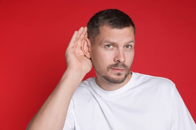 Photo of Man showing hand to ear gesture on red background