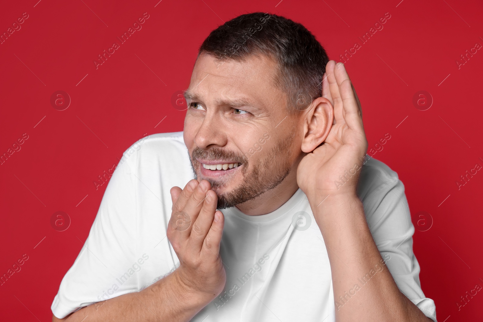 Photo of Man showing hand to ear gesture on red background