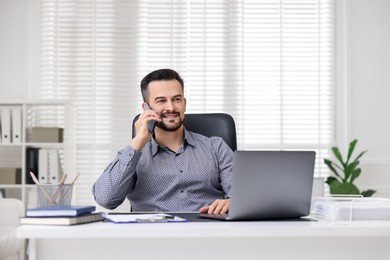 Photo of Happy banker talking on phone at table in office