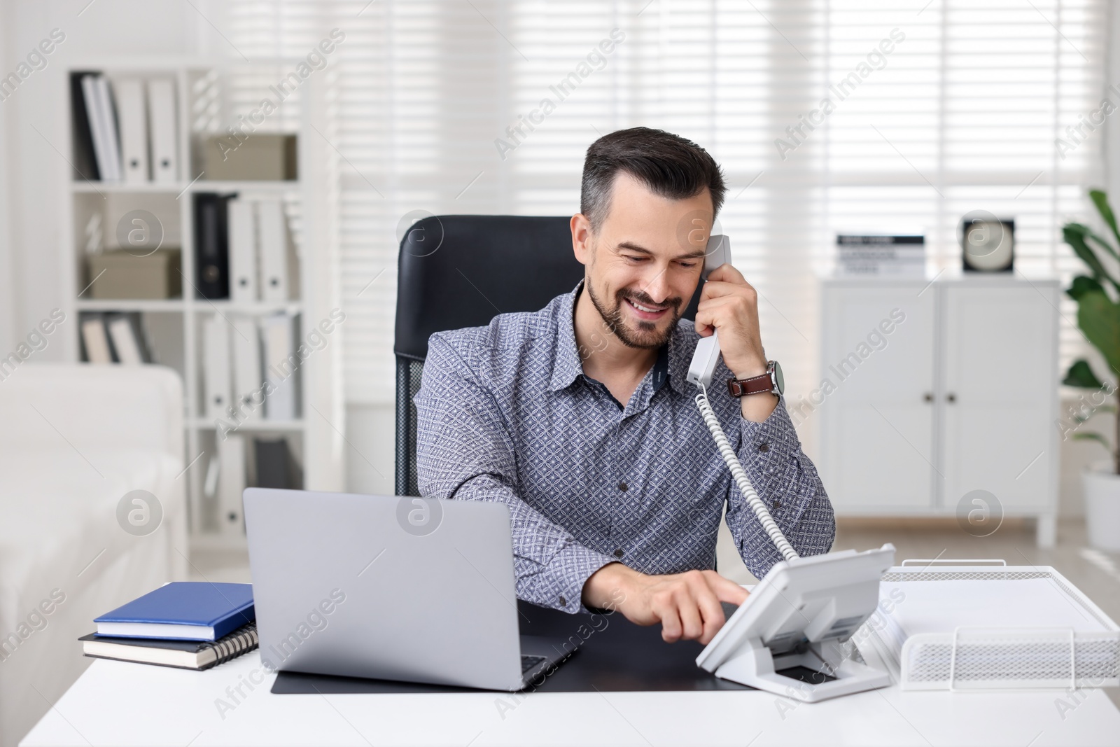 Photo of Happy banker talking on phone at table in office