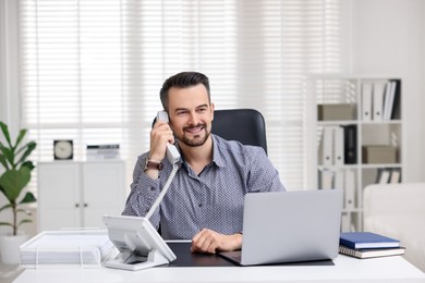 Photo of Happy banker talking on phone at table in office