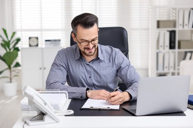 Photo of Handsome banker signing document at table in office