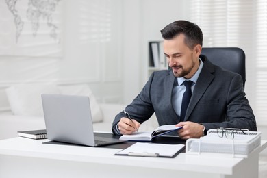 Photo of Handsome banker making notes at table in office