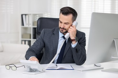 Photo of Handsome banker talking on phone at table in office