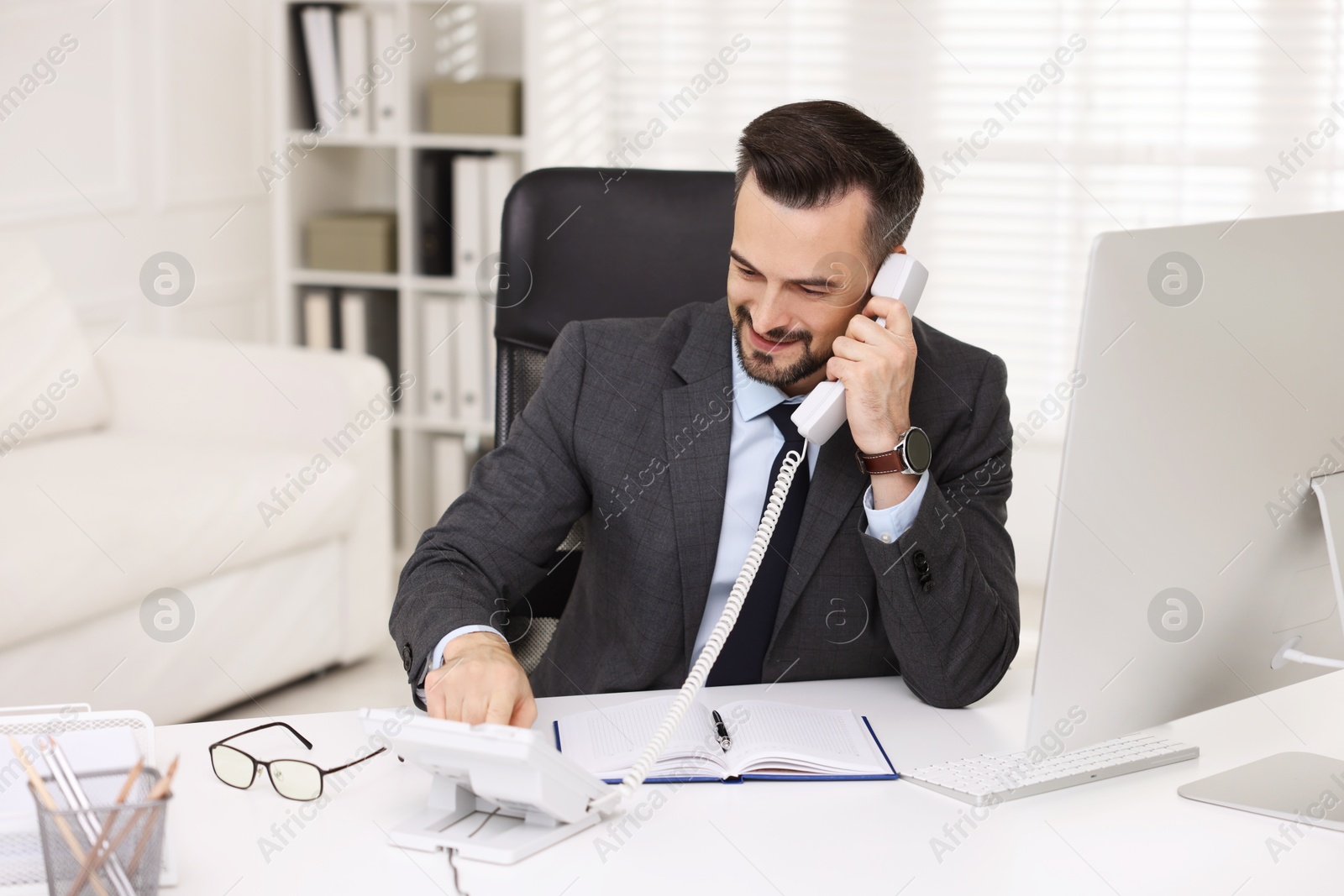 Photo of Happy banker talking on phone at table in office