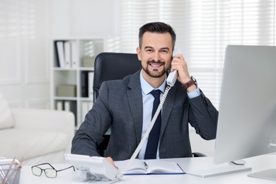 Photo of Happy banker talking on phone at table in office