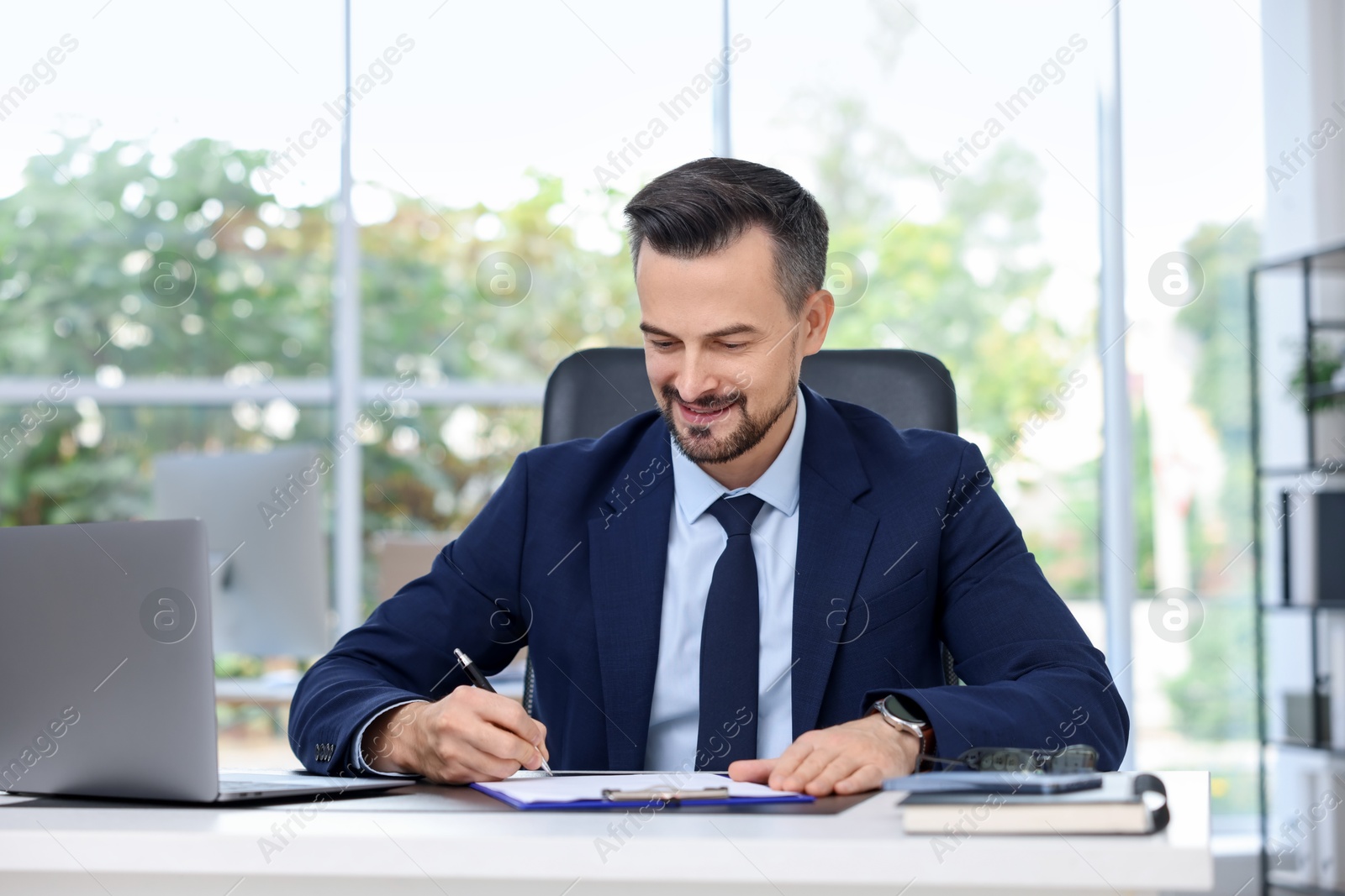 Photo of Handsome banker making notes at table in office