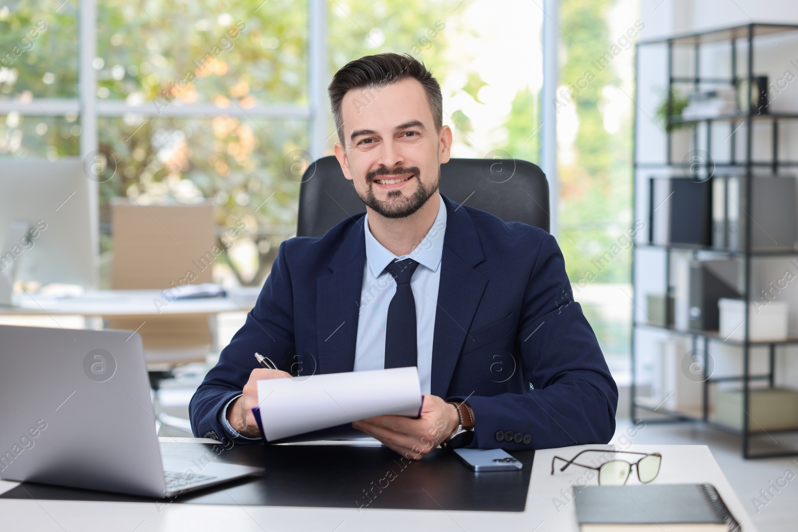 Photo of Happy banker signing document at table in office