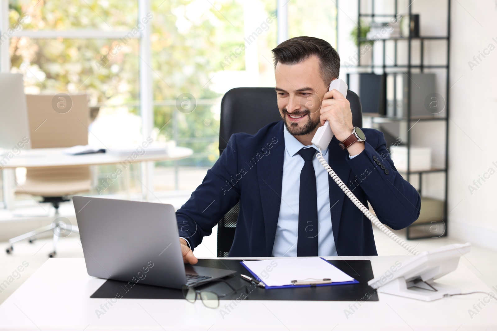 Photo of Happy banker talking on phone at table in office