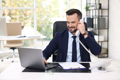 Photo of Happy banker talking on phone at table in office