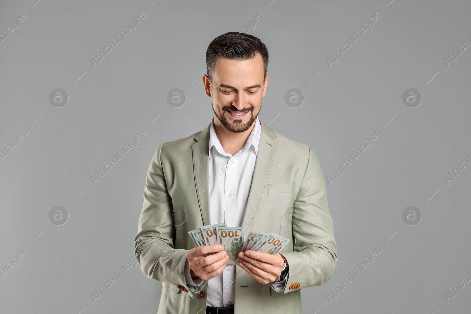 Photo of Portrait of smiling banker counting dollar banknotes on grey background