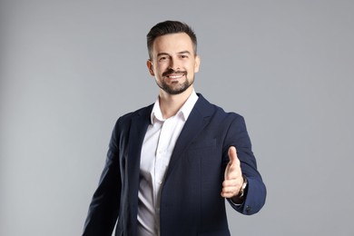 Photo of Portrait of smiling banker offering handshake on grey background