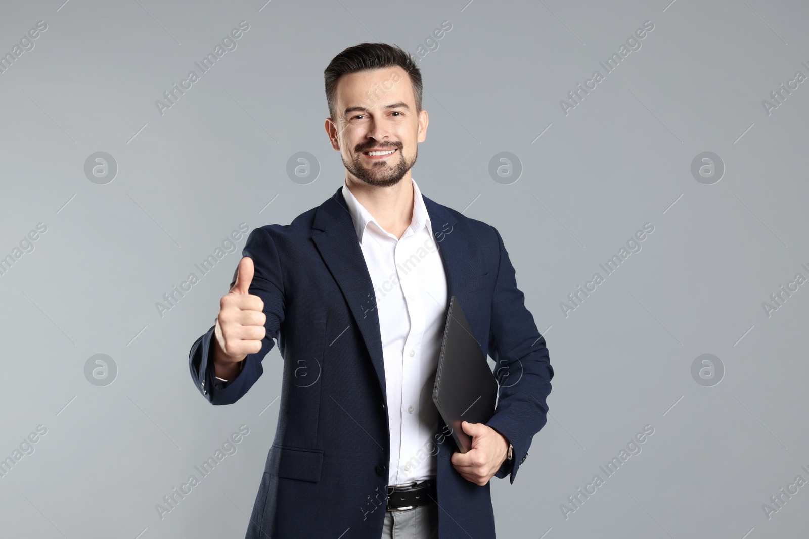 Photo of Portrait of smiling banker with laptop showing thumbs up on grey background