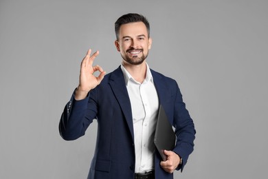 Photo of Portrait of smiling banker with laptop showing ok gesture on grey background