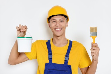 Photo of Portrait of young decorator with paint bucket and brush on white background