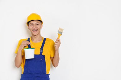 Photo of Portrait of young decorator with paint bucket and brush on white background, space for text