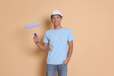 Photo of Portrait of young decorator with paint roller on beige background