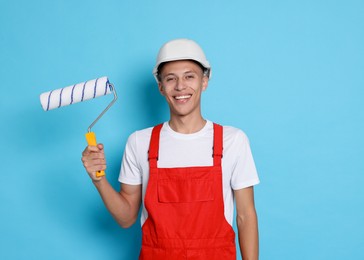 Photo of Portrait of young decorator with paint roller on light blue background