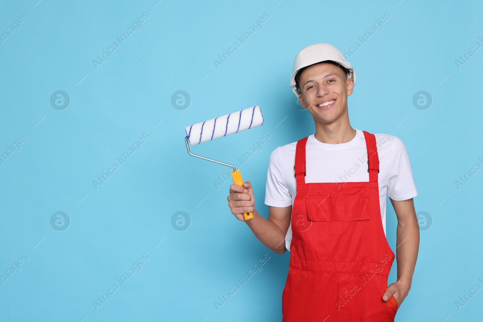 Photo of Portrait of young decorator with paint roller on light blue background, space for text