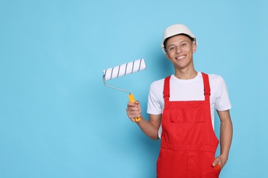 Photo of Portrait of young decorator with paint roller on light blue background, space for text