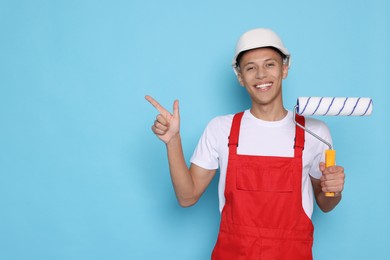 Photo of Portrait of young decorator with paint roller on light blue background, space for text