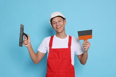 Photo of Portrait of young decorator with putty knives on light blue background