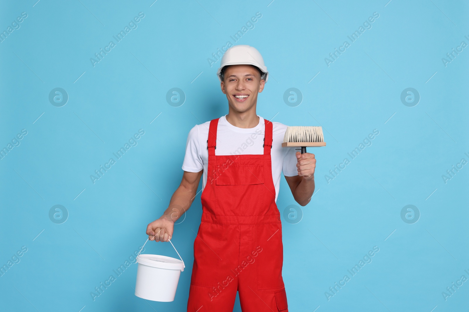 Photo of Portrait of young decorator with bucket and brush on light blue background